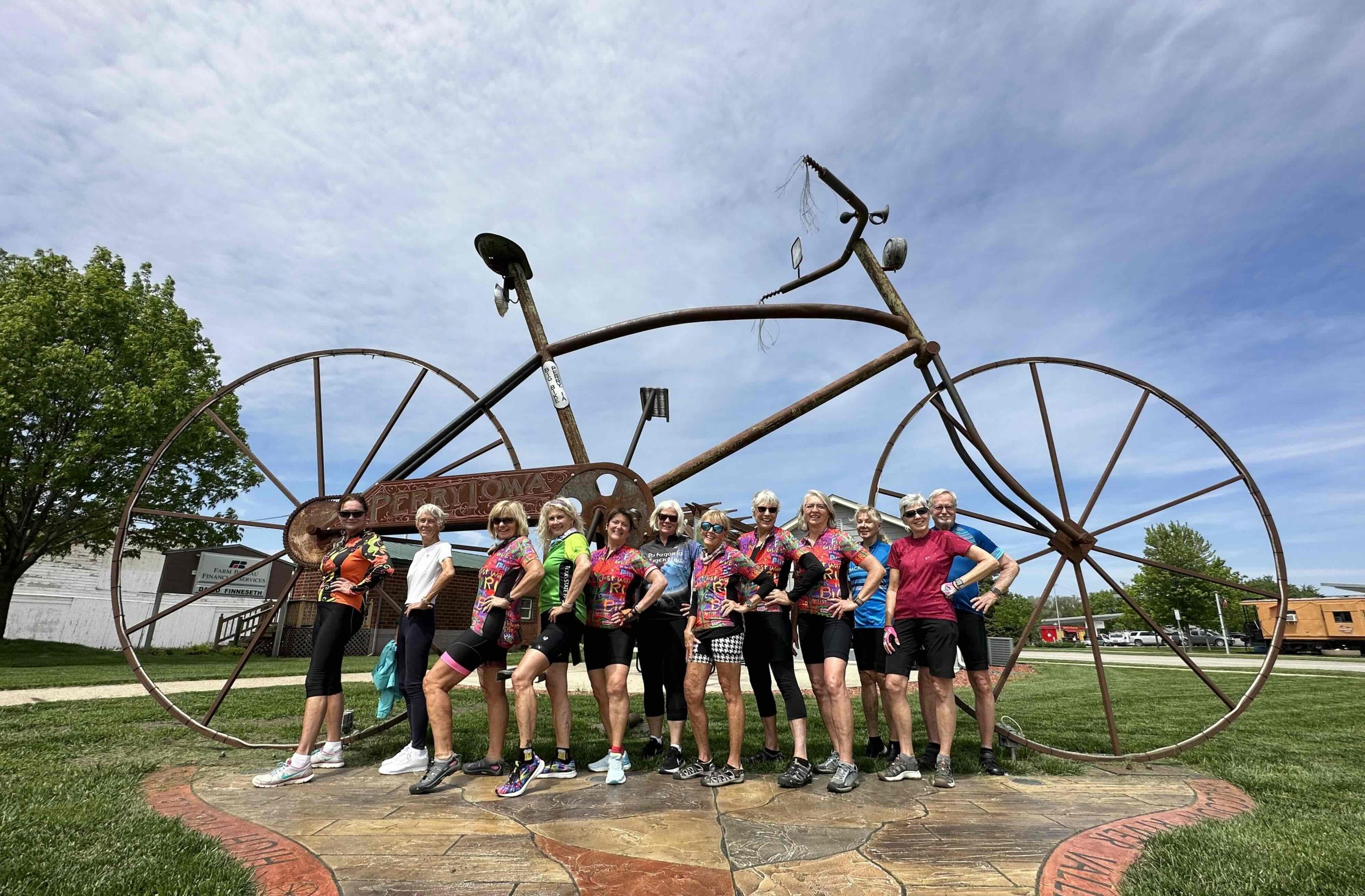 A bunch of women cyclists posing in front of a bike statue.