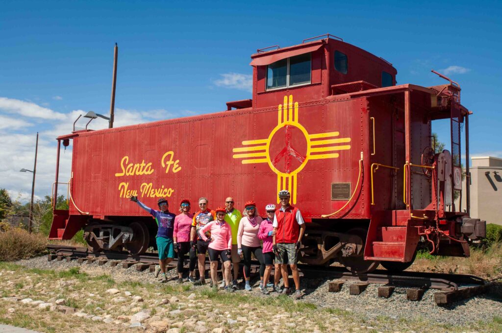 A group of cyclists posing in front of the Red Caboose along a rail trail in Santa Fe, New Mexico.